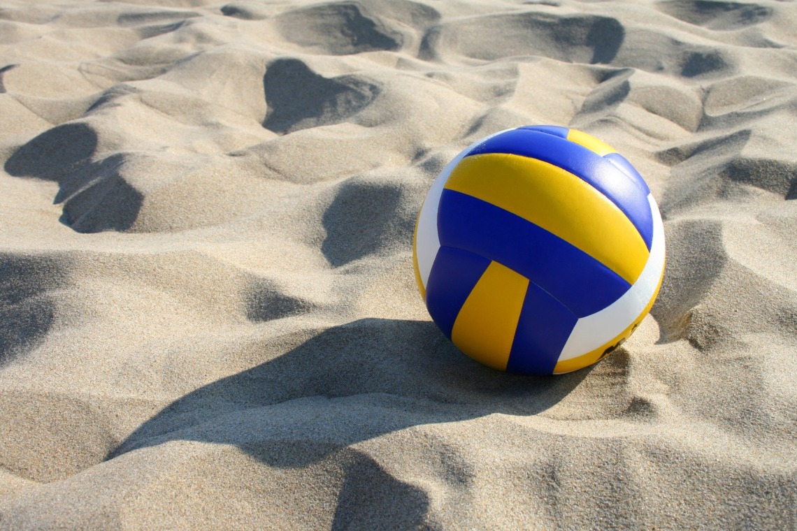 Yellow, blue, and white volleyball sitting in the sand