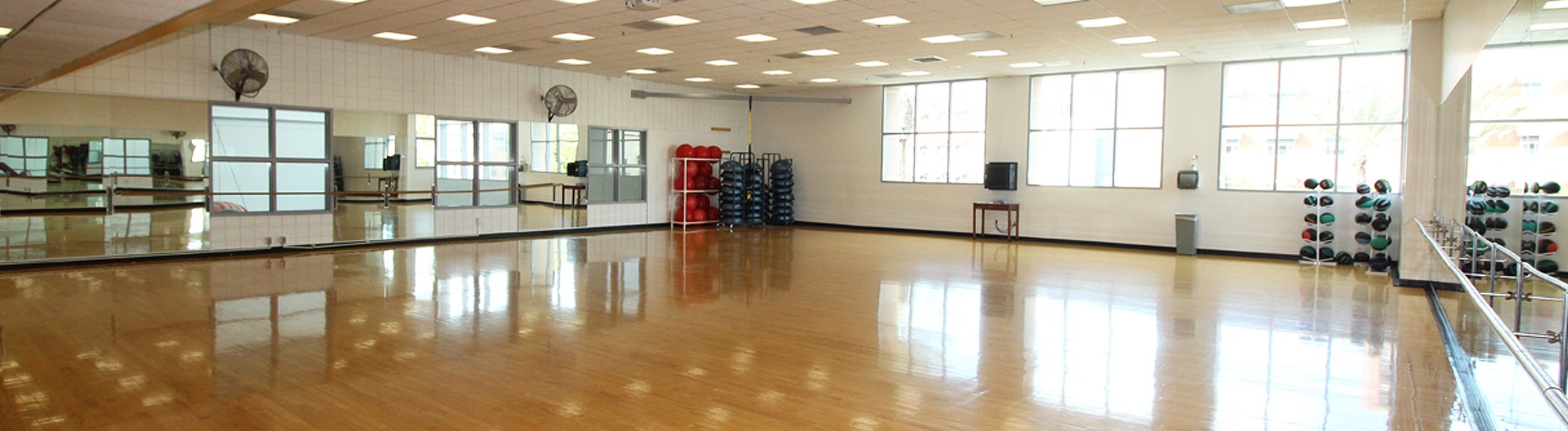 Multipurpose studio with wood floors and mirrors, fitness equipment agains the walls