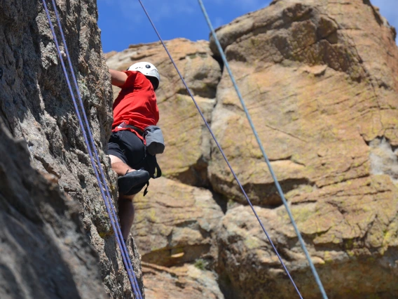 Climber scaling cliff wall, belay lines in foreground