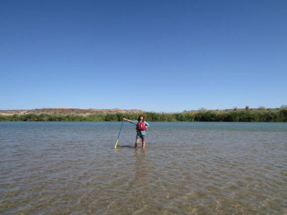 Canoer standing in water with paddle in hand, other hand on hip