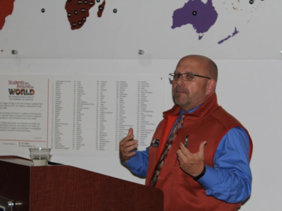 Troy Vaughn giving speech in front of "students from around the world" display