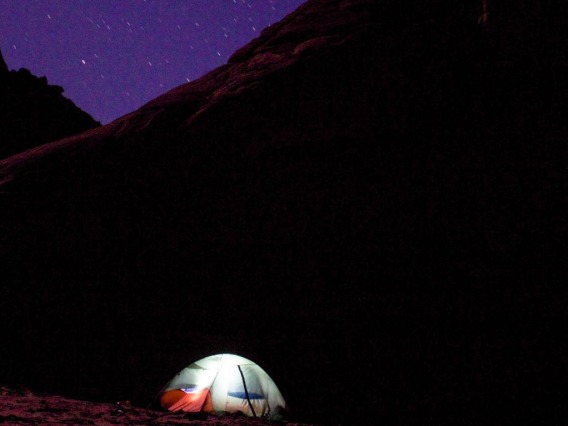 Tent illuminated from inside, dark mountains and stars in background