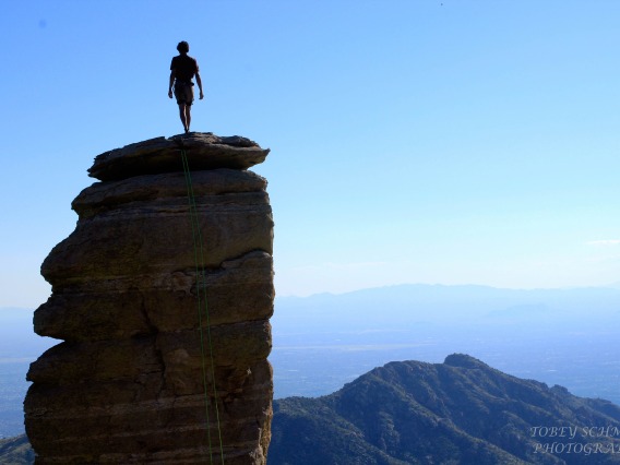 Rock climber standing with back to camera, atop a rock peak