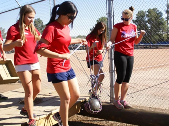 Group of people completing challenge course by carrying a weight across a clearing