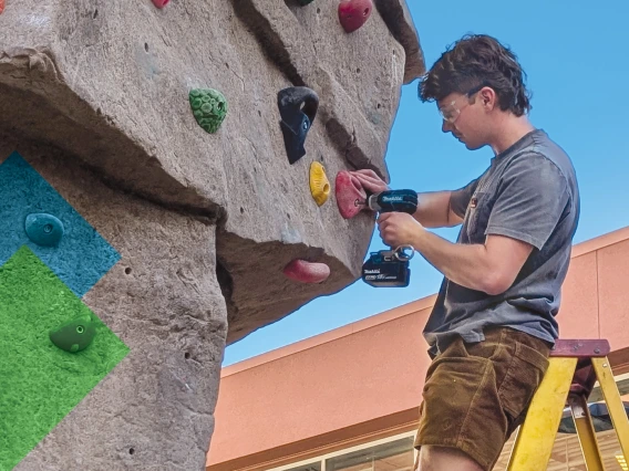 Male route-setter on ladder, installing a climbing route on bouldering wall