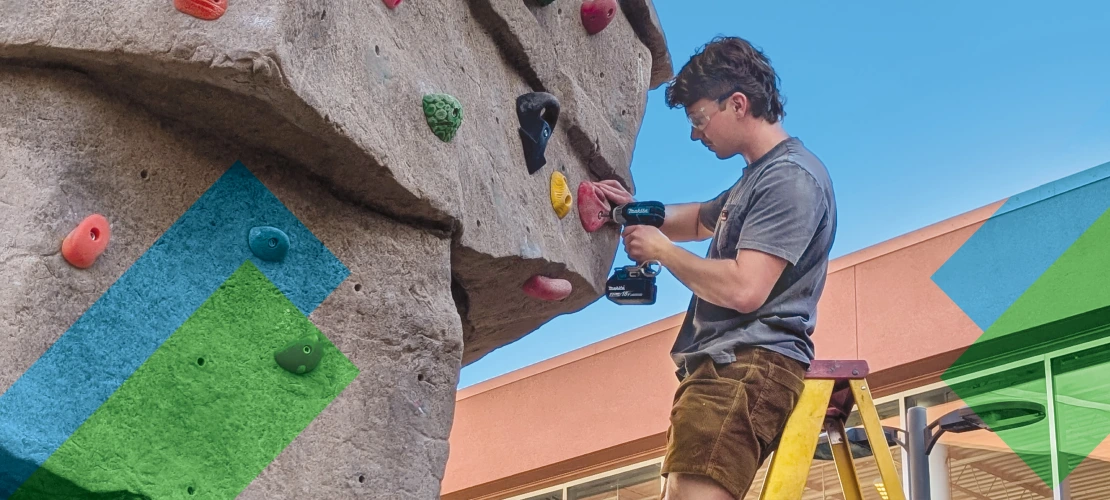 Male route-setter on ladder, installing a climbing route on bouldering wall