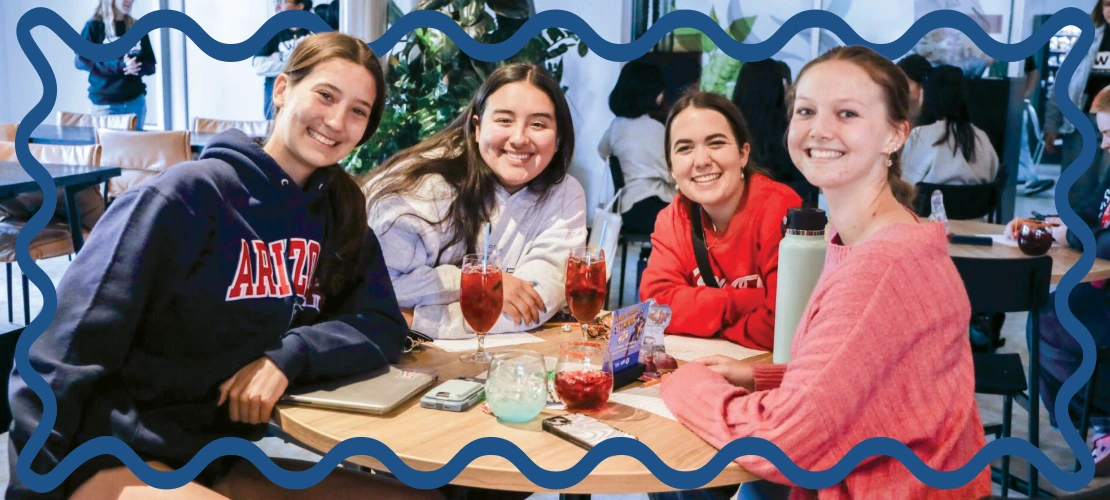 Four female students smiling, sitting at a table.