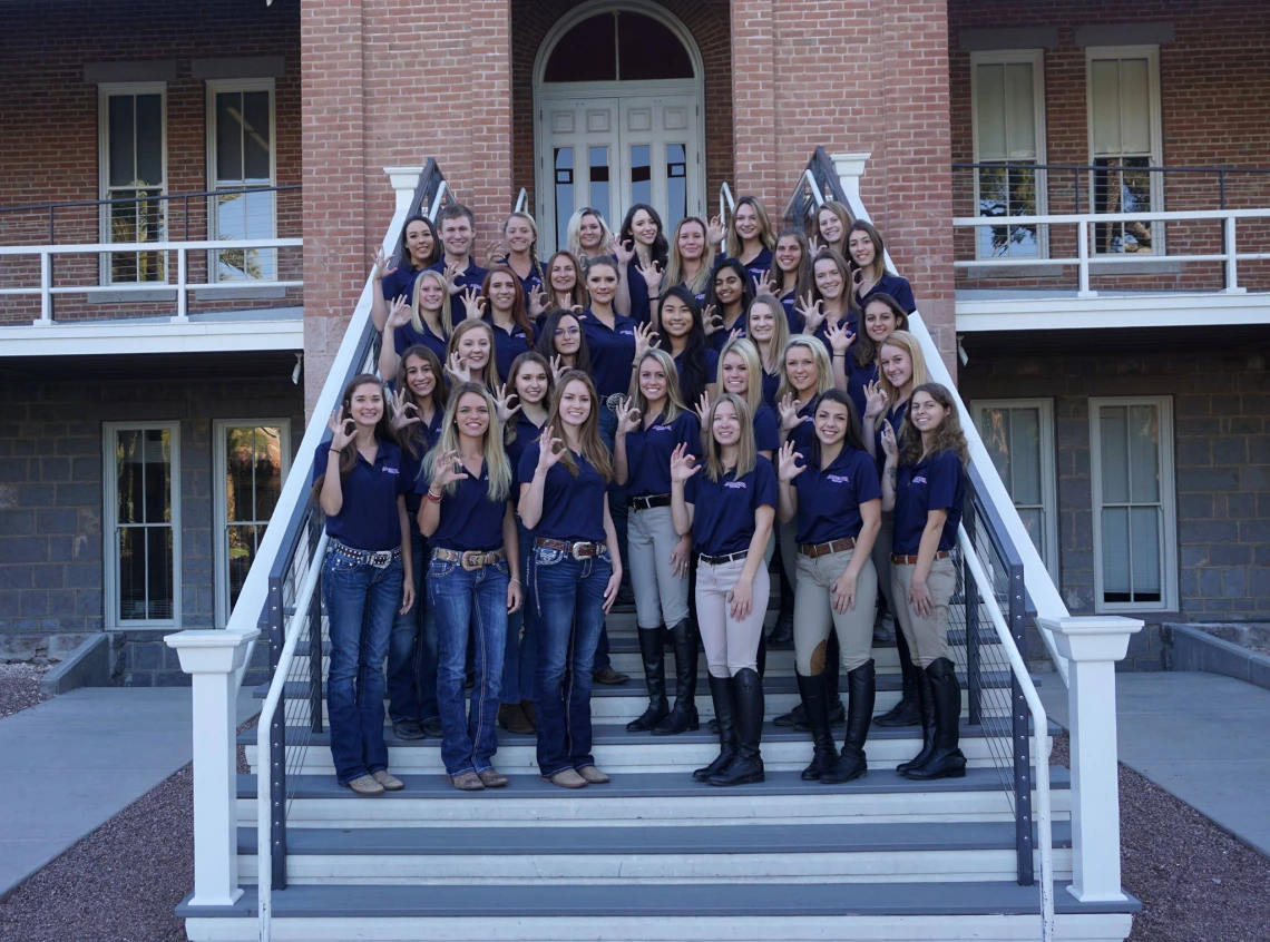 Equestrian team standing on Old Main steps, making letter "c" with their fingers