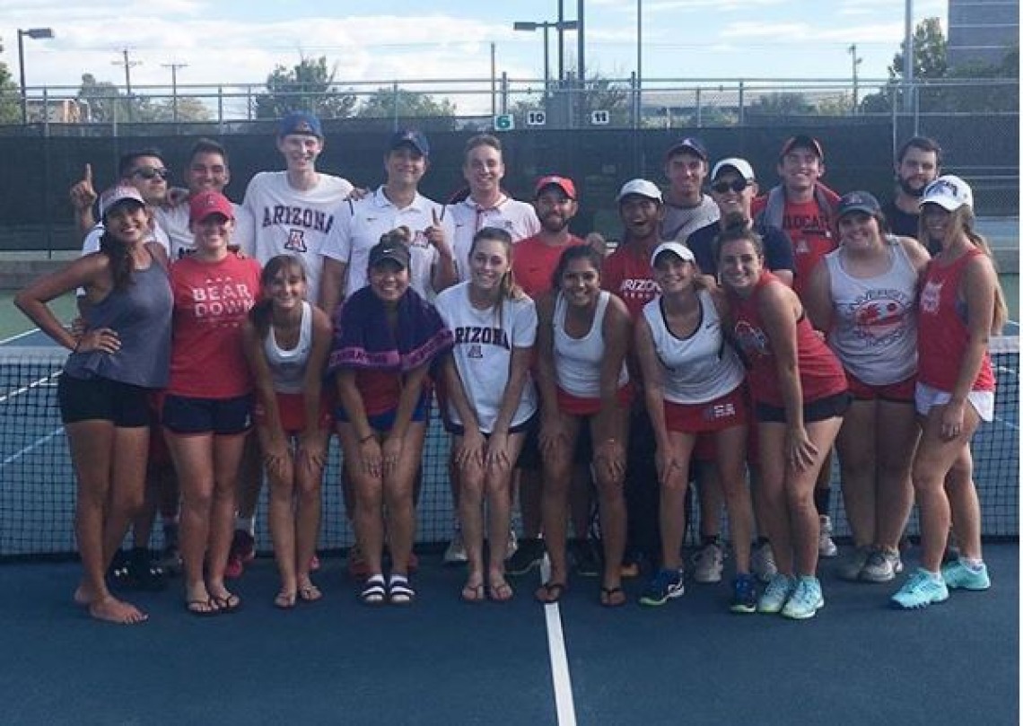 Tennis team posing for photo on tennis court, in front of net