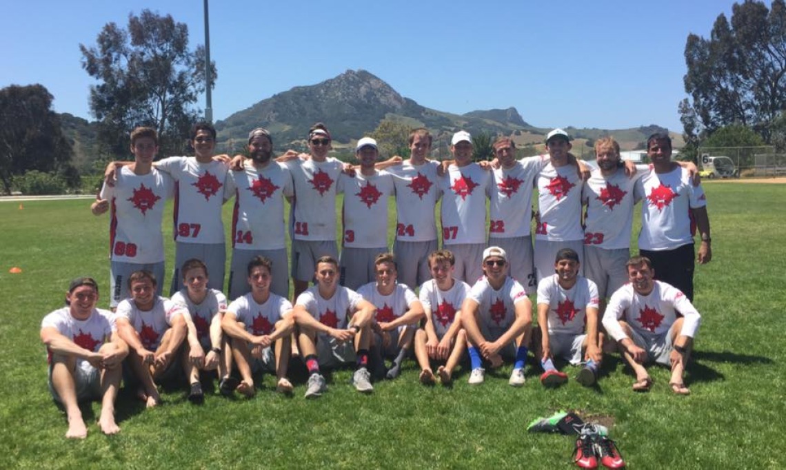 Men's Ultimate team posing for photo in grass, mountains in background