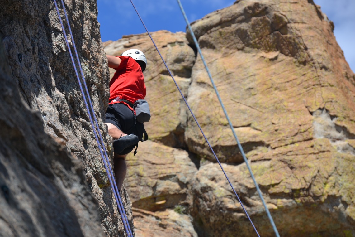Climber scaling cliff wall, belay lines in foreground