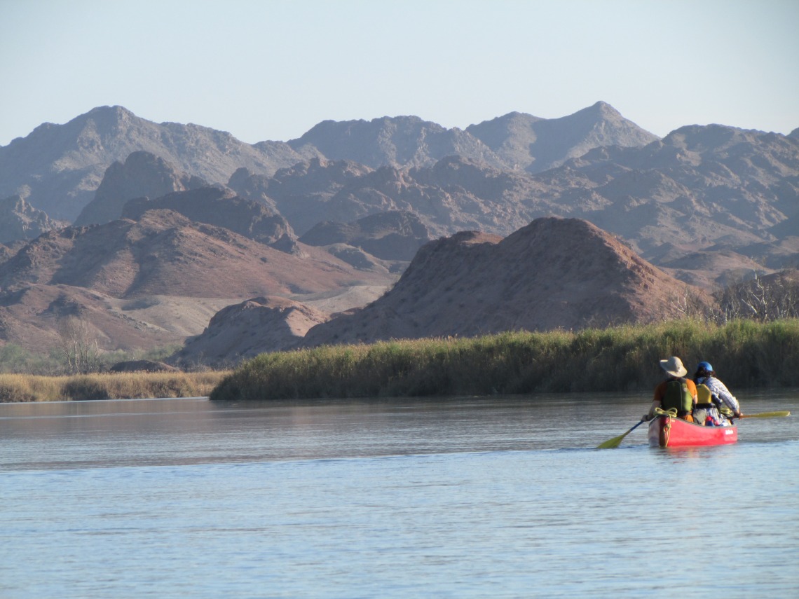 Canoe paddling through water with mountains in background