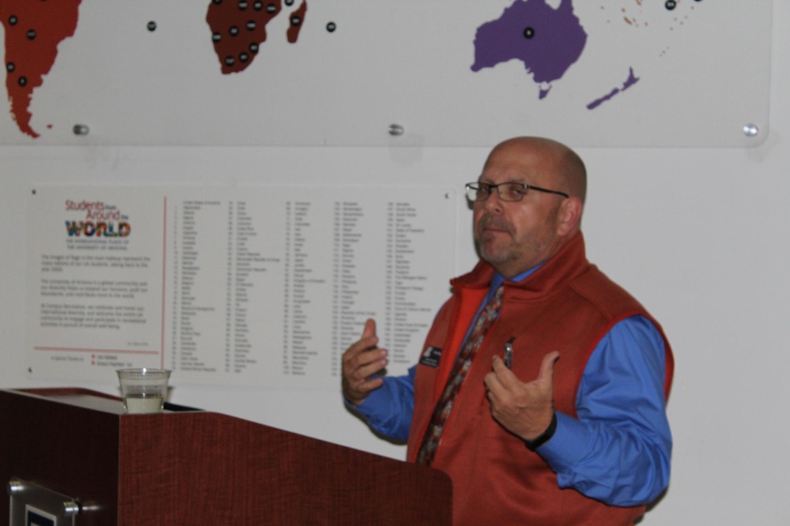 Troy Vaughn giving speech in front of "students from around the world" display
