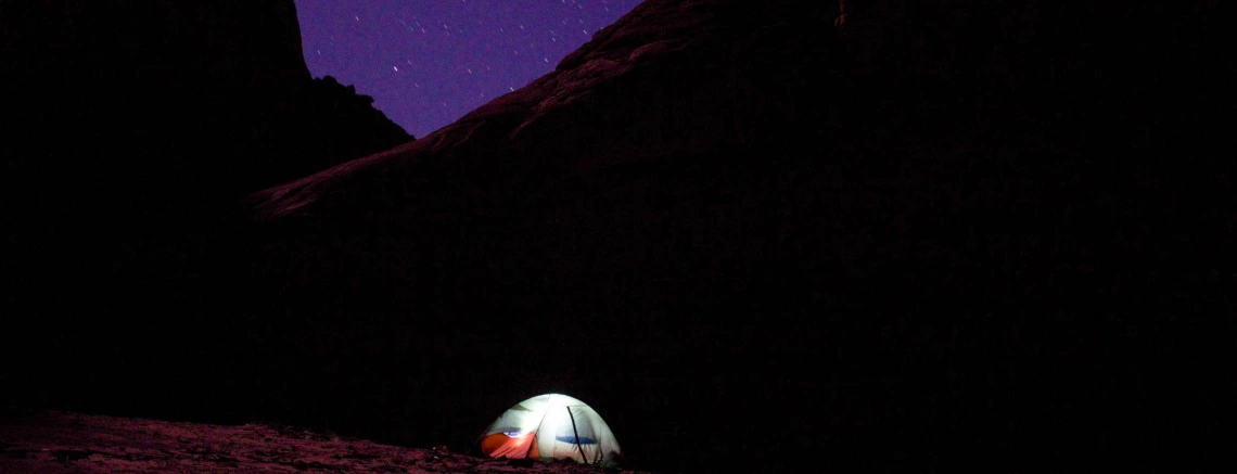 Tent illuminated from inside, dark mountains and stars in background