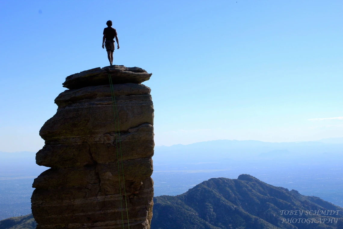 Rock climber standing with back to camera, atop a rock peak