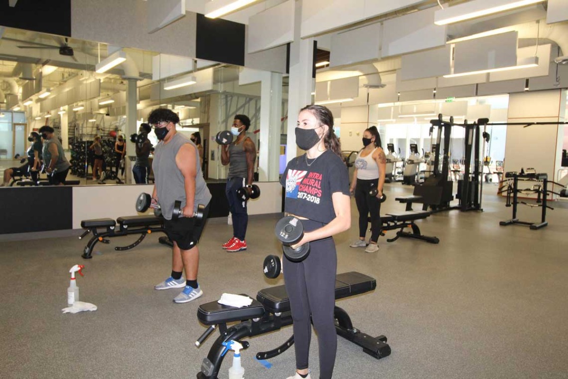 Patrons socially distanced while using free weights, cleaning spray close by