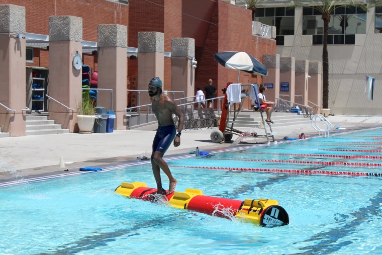 Young man balancing on log in swimming pool.