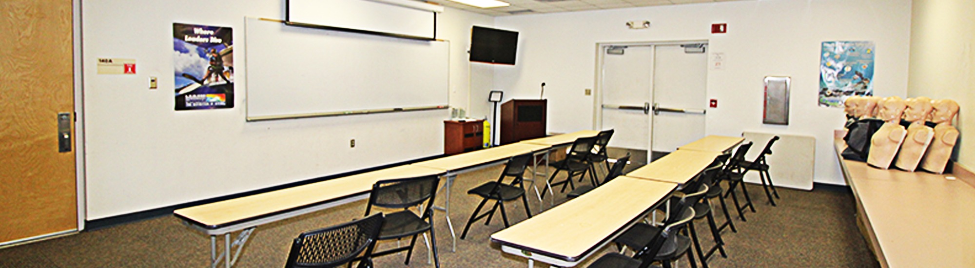 Conference room with tables, chairs, white boards, and CPR training dummies.