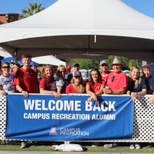 Crowd of people standing at tailgate behind poster that reads: Welcome Back Campus Recreation Alumni.